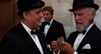 Movie still from “The Producers” (1967), directed by Mel Brooks – Two men in tuxedos and hats looking at a piece of paper; Medium shot, Over the shoulder angle