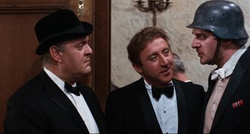 Movie still from “The Producers” (1967), directed by Mel Brooks – A group of men standing next to each other wearing tuxedos; Medium shot, Over the shoulder angle