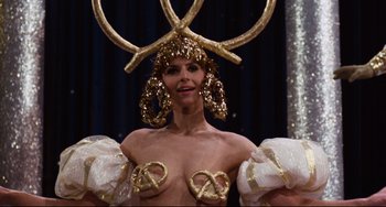Movie still from “The Producers” (1967), directed by Mel Brooks – A woman in a gold costume with pretzels on top of her head; Close Up shot, Over the shoulder angle