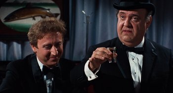 Movie still from “The Producers” (1967), directed by Mel Brooks – Two men in tuxedos and hats are holding glasses of wine; Medium shot, Over the shoulder angle