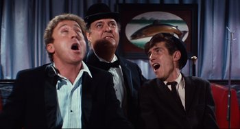 Movie still from “The Producers” (1967), directed by Mel Brooks – A group of men in suits and hats singing together; Medium shot, Low angle
