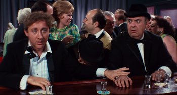 Movie still from “The Producers” (1967), directed by Mel Brooks – A group of people sitting at a table with drinks in front of them; Medium shot, Over the shoulder angle