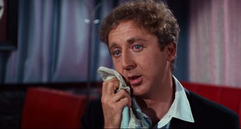 Movie still from “The Producers” (1967), directed by Mel Brooks – A person holding a towel over their face; Close Up shot, Over the shoulder angle