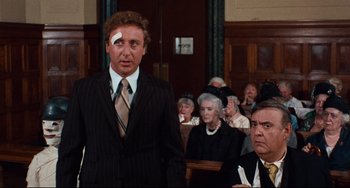 Movie still from “The Producers” (1967), directed by Mel Brooks – A man with a bandage on his head stands in front of an audience; Medium shot, Over the shoulder angle
