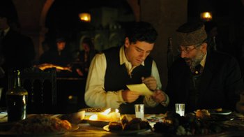 Movie still from “The Promise” (2016), directed by Terry George – A man sitting at a dinner table writing on a piece of paper; Medium shot, Over the shoulder angle