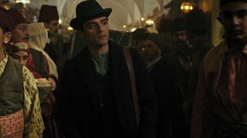 Movie still from “The Promise” (2016), directed by Terry George – A man wearing a black hat and a black coat; Medium shot, Over the shoulder angle