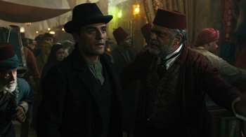 Movie still from “The Promise” (2016), directed by Terry George – A man in a hat standing next to another man in a hat; Medium shot, Over the shoulder angle
