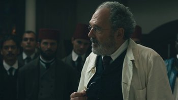 Movie still from “The Promise” (2016), directed by Terry George – An older man in a suit and tie; Medium shot, Over the shoulder angle