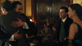 Movie still from “The Promise” (2016), directed by Terry George – Two men hugging in a room with people in the background; Medium shot, Over the shoulder angle
