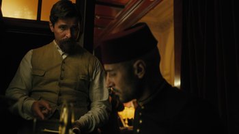 Movie still from “The Promise” (2016), directed by Terry George – Two men sitting at a table in front of each other; Medium shot, Over the shoulder angle