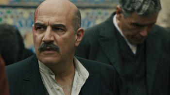 Movie still from “The Promise” (2016), directed by Terry George – A man in a suit and tie with a bald head; Close Up shot, Over the shoulder angle