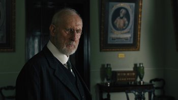 Movie still from “The Promise” (2016), directed by Terry George – An older man wearing a suit and tie in front of a painting; Close Up shot, Over the shoulder angle