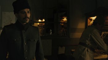 Movie still from “The Promise” (2016), directed by Terry George – A man in a uniform standing next to another man; Medium shot, Low angle