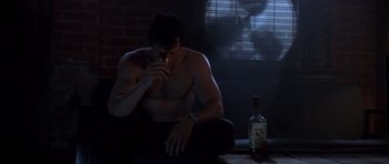 Movie still from “The Punisher” (2004), directed by Jonathan Hensleigh – A shirtless man sitting in front of a bottle of alcohol; Medium shot, Low angle