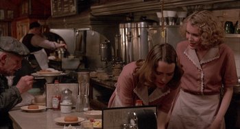 Movie still from “The Purple Rose of Cairo” (1985), directed by Woody Allen – A woman in a pink shirt is in a kitchen; Medium shot, Over the shoulder angle