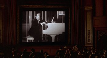 Movie still from “The Purple Rose of Cairo” (1985), directed by Woody Allen – A man in a black suit is on a large screen in a theater; Wide shot, High angle