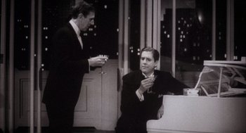 Movie still from “The Purple Rose of Cairo” (1985), directed by Woody Allen – A man sitting next to another man holding a cigarette; Medium shot, High angle