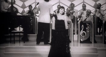 Movie still from “The Purple Rose of Cairo” (1985), directed by Woody Allen – A black and white photo of a woman in front of an orchestra; Medium shot, Low angle