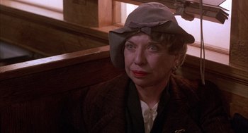 Movie still from “The Purple Rose of Cairo” (1985), directed by Woody Allen – An older woman wearing a hat sitting on a bench; Close Up shot, Over the shoulder angle