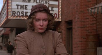 Movie still from “The Purple Rose of Cairo” (1985), directed by Woody Allen – A woman wearing a brown coat and a brown hat standing in front of a movie theater; Close Up shot, Low angle