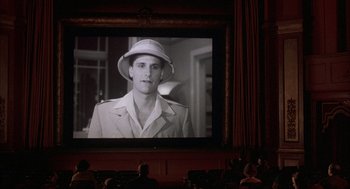 Movie still from “The Purple Rose of Cairo” (1985), directed by Woody Allen – A man wearing a hat is shown on a large screen; Wide shot, Low angle