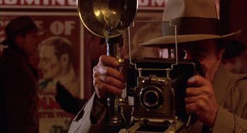 Movie still from “The Purple Rose of Cairo” (1985), directed by Woody Allen – A man holding an old fashioned camera and a light; Close Up shot, Low angle