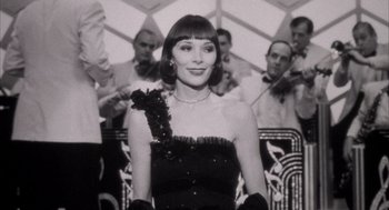 Movie still from “The Purple Rose of Cairo” (1985), directed by Woody Allen – A black and white photo of a woman in a black dress; Medium shot, Low angle
