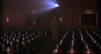Movie still from “The Purple Rose of Cairo” (1985), directed by Woody Allen – A man standing in front of rows of chairs in an auditorium; Wide shot, Low angle