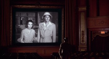 Movie still from “The Purple Rose of Cairo” (1985), directed by Woody Allen – A man standing in front of a big screen tv; Wide shot, Low angle