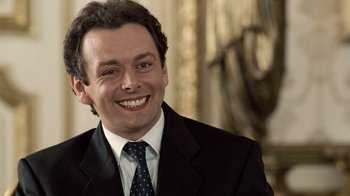 Movie still from “The Queen” (2006), directed by Stephen Frears – A man wearing a suit and tie smiling for the camera; Close Up shot, High angle
