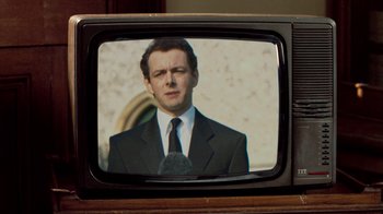 Movie still from “The Queen” (2006), directed by Stephen Frears – A man wearing a suit and tie on a television screen; Close Up shot, Over the shoulder angle