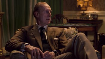 Movie still from “The Queen” (2006), directed by Stephen Frears – An older man in a suit and tie sitting in a chair; Medium shot, Low angle