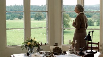 Movie still from “The Queen” (2006), directed by Stephen Frears – An older woman standing in front of a window looking out at a field; Medium shot, Over the shoulder angle