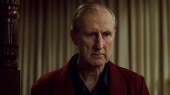 Movie still from “The Queen” (2006), directed by Stephen Frears – An older man wearing a red jacket looking at the camera; Close Up shot, Low angle