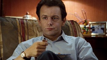 Movie still from “The Queen” (2006), directed by Stephen Frears – A man sitting on a couch holding a pen; Close Up shot, High angle