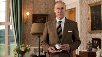 Movie still from “The Queen” (2006), directed by Stephen Frears – An older man in a brown suit holding a cup; Medium shot, Low angle