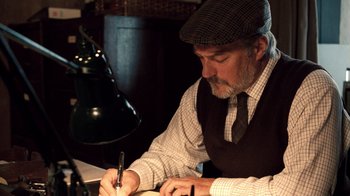 Movie still from “The Queen” (2006), directed by Stephen Frears – A man writing on a piece of paper in front of a lamp; Medium shot, Low angle