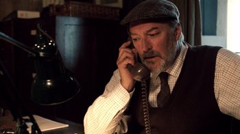 Movie still from “The Queen” (2006), directed by Stephen Frears – An older man talking on a phone while wearing a hat; Close Up shot, Low angle