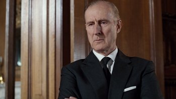 Movie still from “The Queen” (2006), directed by Stephen Frears – An older man wearing a suit and tie with his arms crossed; Close Up shot, Low angle