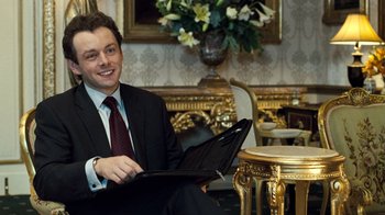 Movie still from “The Queen” (2006), directed by Stephen Frears – A man in a suit and tie sitting in front of an open laptop computer; Medium shot, High angle