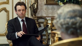 Movie still from “The Queen” (2006), directed by Stephen Frears – A man in a suit and tie holding a laptop; Medium shot, Over the shoulder angle