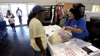 Movie still from “The Queen of Versailles” (2012), directed by Lauren Greenfield – A woman in a blue hat is handing a bag to a woman; Medium shot, Over the shoulder angle