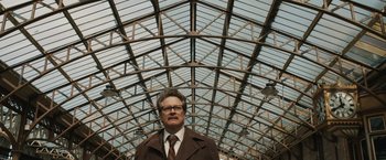 Movie still from “The Railway Man” (2013), directed by Jonathan Teplitzky – A man in a brown coat standing under a glass ceiling; Medium shot, Low angle