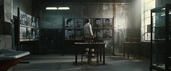 Movie still from “The Railway Man” (2013), directed by Jonathan Teplitzky – A man sitting at a table in front of a bunch of pictures; Wide shot, Over the shoulder angle