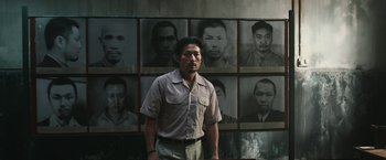 Movie still from “The Railway Man” (2013), directed by Jonathan Teplitzky – A man standing in front of a group of pictures; Medium shot, High angle