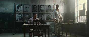 Movie still from “The Railway Man” (2013), directed by Jonathan Teplitzky – Two men sitting at a table in front of a wall of photos; Wide shot, Over the shoulder angle
