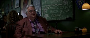 Movie still from “The Rainmaker” (1997), directed by Francis Ford Coppola – An older man sitting at a table with a glass of wine; Medium shot, Low angle