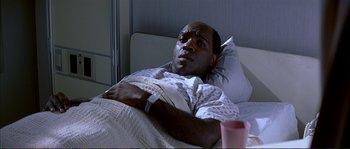 Movie still from “The Rainmaker” (1997), directed by Francis Ford Coppola – A man laying in a hospital bed with a cup in his hand; Medium shot, High angle