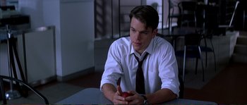 Movie still from “The Rainmaker” (1997), directed by Francis Ford Coppola – A man sitting at a table holding an apple; Medium shot, Over the shoulder angle