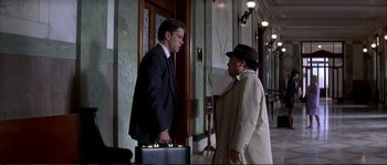 Movie still from “The Rainmaker” (1997), directed by Francis Ford Coppola – A man in a suit and a man in a hat talking to each other in a hallway; Medium shot, Over the shoulder angle